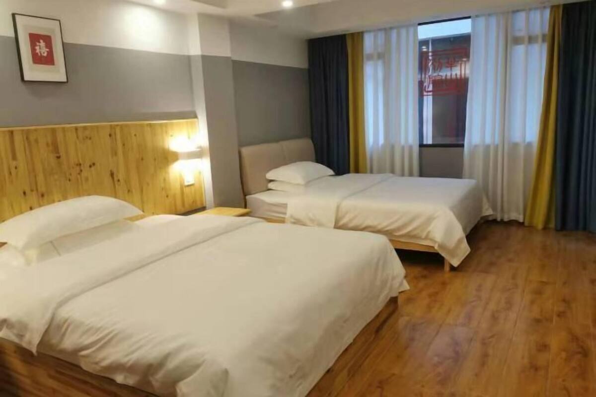 Habitación de hotel con dos camas, cabecero de madera, lámparas de noche y un gran ventanal con cortinas.