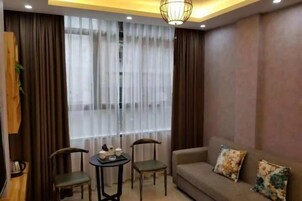 Una habitación con sofá, dos sillones, una mesita con objetos y un ventanal con cortinas.