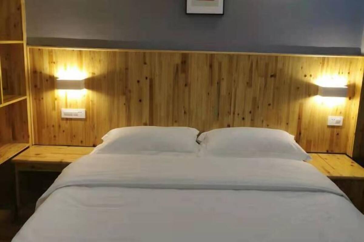 Cabecera de madera con dos lámparas de pared, una cama con ropa blanca de cama y una mesita de noche pequeña.