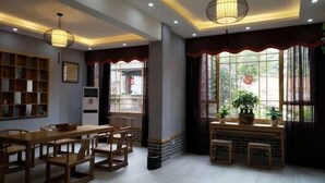 A dining area with a long wooden table and chairs, a bookshelf, and a window with curtains. - Banshan Bieyuan Inn (Yanjin)