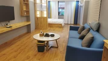 Ein Zimmer mit einem Bett, einem blauen Sofa, einem Fernseher, einer Holzablage und einem kleinen Tisch mit einem Mülleimer.