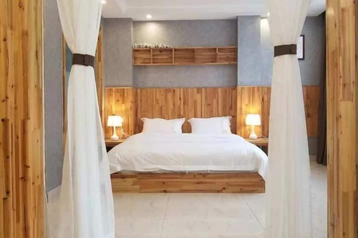 Un dormitorio con cabecera de madera, dos mesitas de noche con lámparas y una cama con ropa blanca de cama.