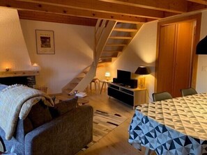 Una sala de estar acogedora con chimenea, una escalera, zona de comedor y televisión.