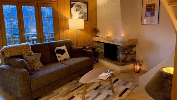 Ein gemütliches Wohnzimmer mit Holzboden, Kamin aus Stein, einer Couch mit Kissen und einer Lampe.