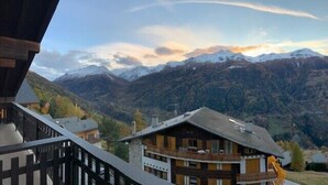 Ein Berggasthof mit einem Balkon mit Blick auf ein Tal und schneebedeckte Berge.