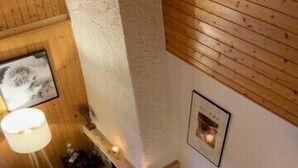 Eine Holztreppe führt zu einem Wohnbereich mit Kamin, einer Couch und einer Lampe.