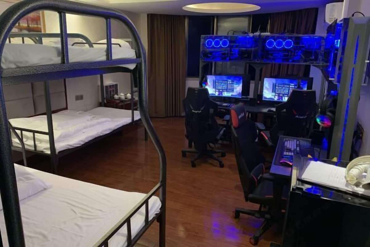 Quarto de hotel com beliches, uma escrivaninha com dois computadores e uma cadeira gamer.