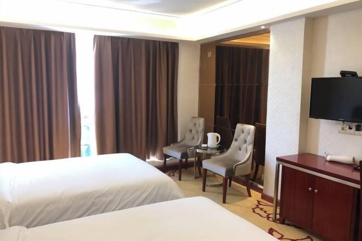 Quarto de hotel com duas camas, uma escrivaninha com cadeira, televisão e um armário.