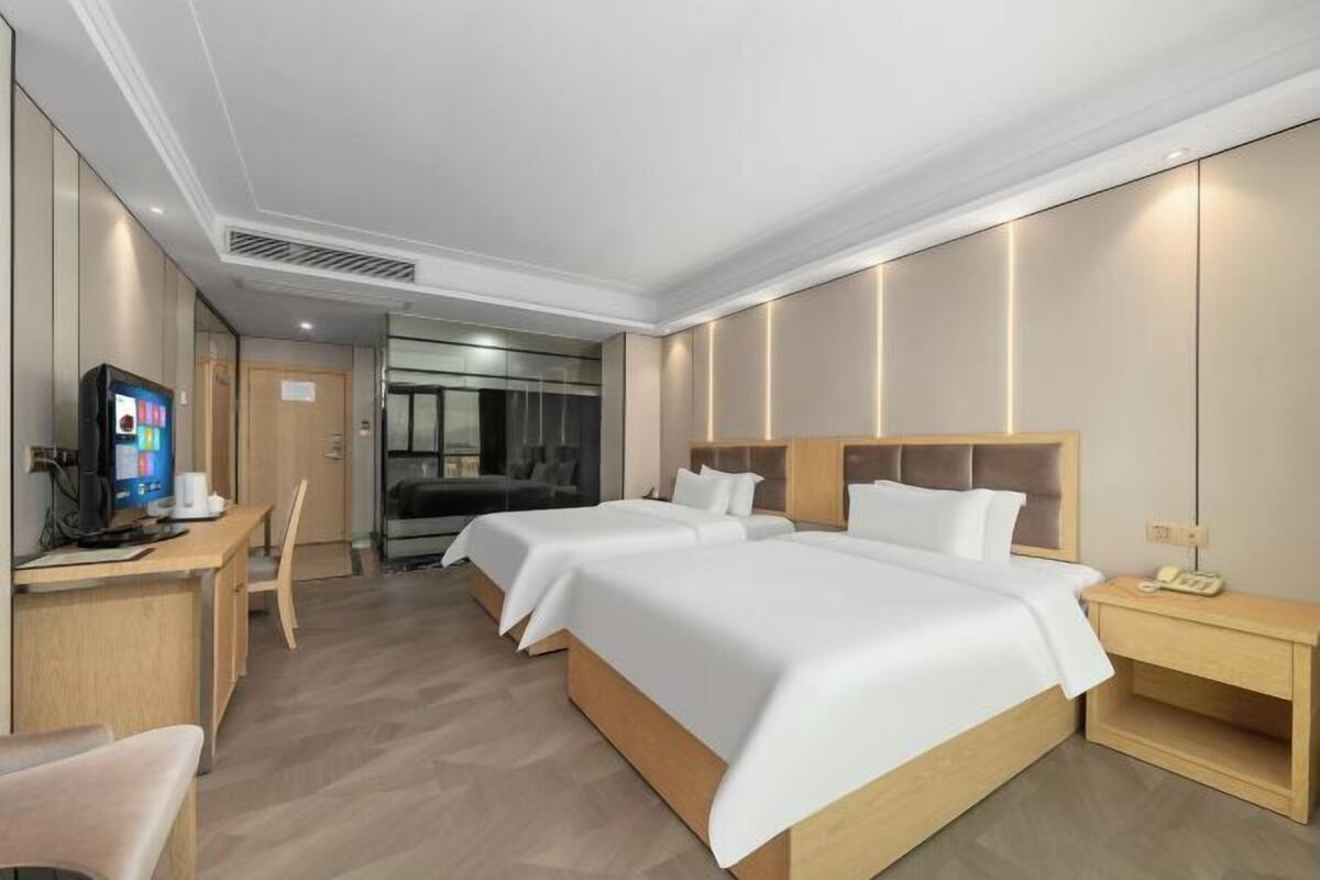 Quarto de hotel com duas camas, uma escrivaninha com computador, uma cadeira e uma televisão.