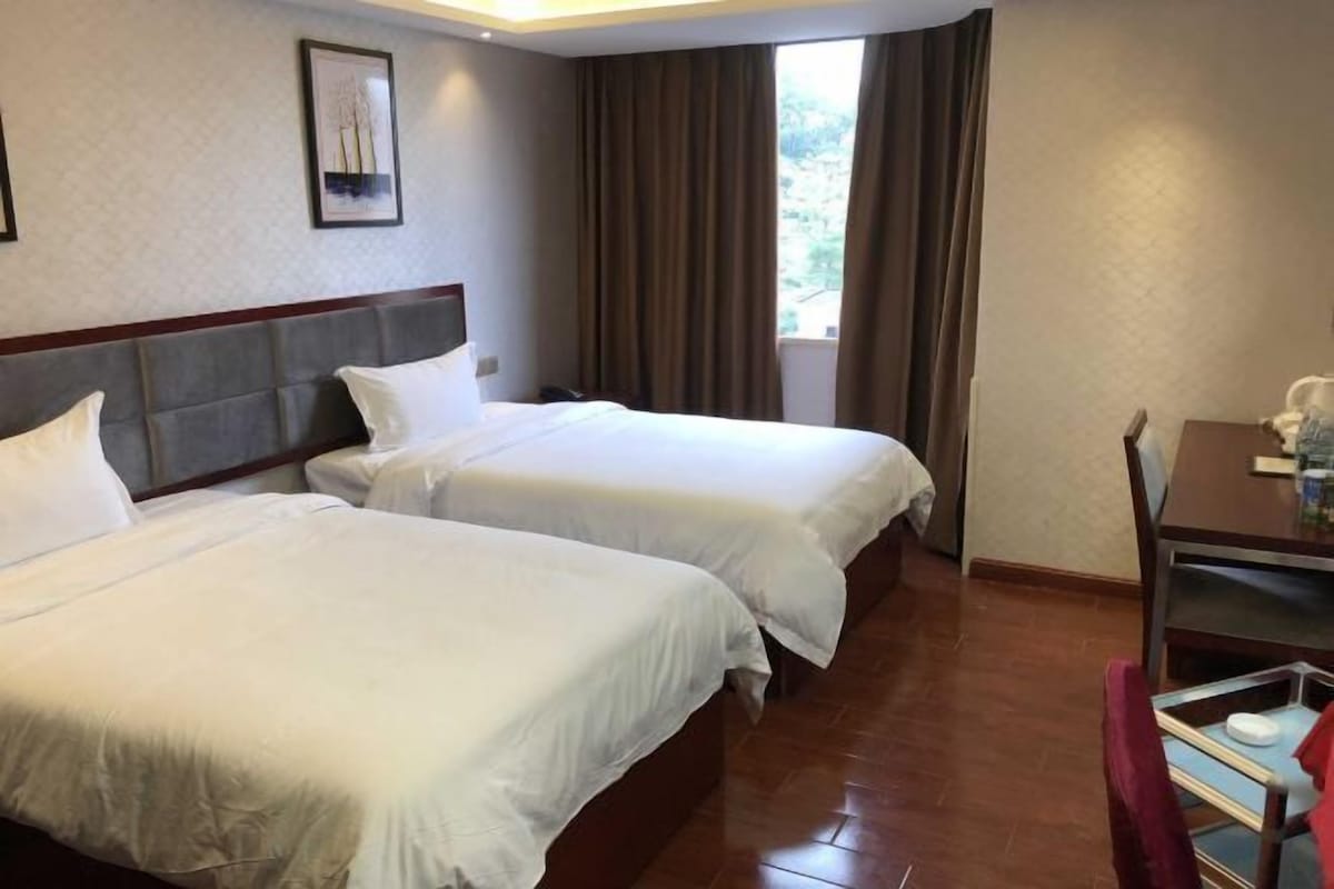 A hotel room with two beds, a dining table, and a window with curtains.