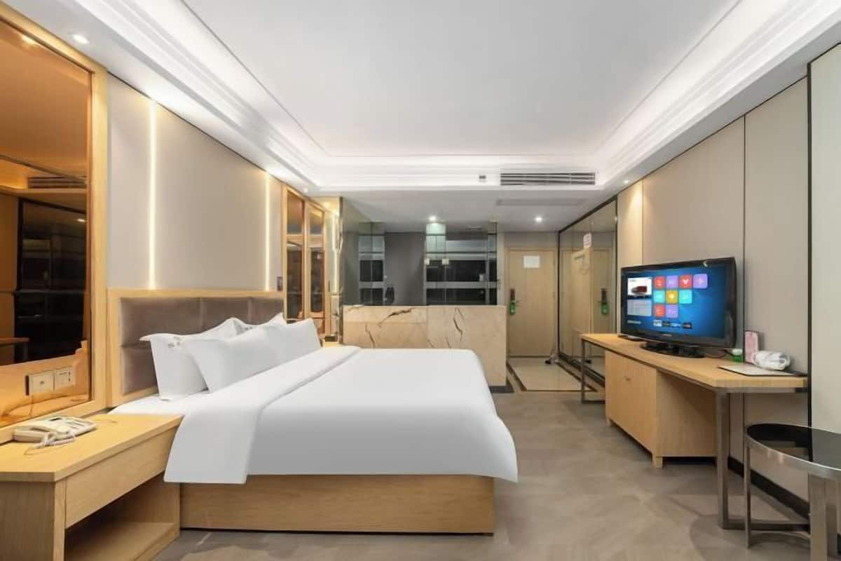Quarto de hotel com cama, mesa de cabeceira, televisão e escrivaninha com cadeira.