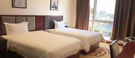 A hotel room with two beds, a desk, and a large window with curtains.