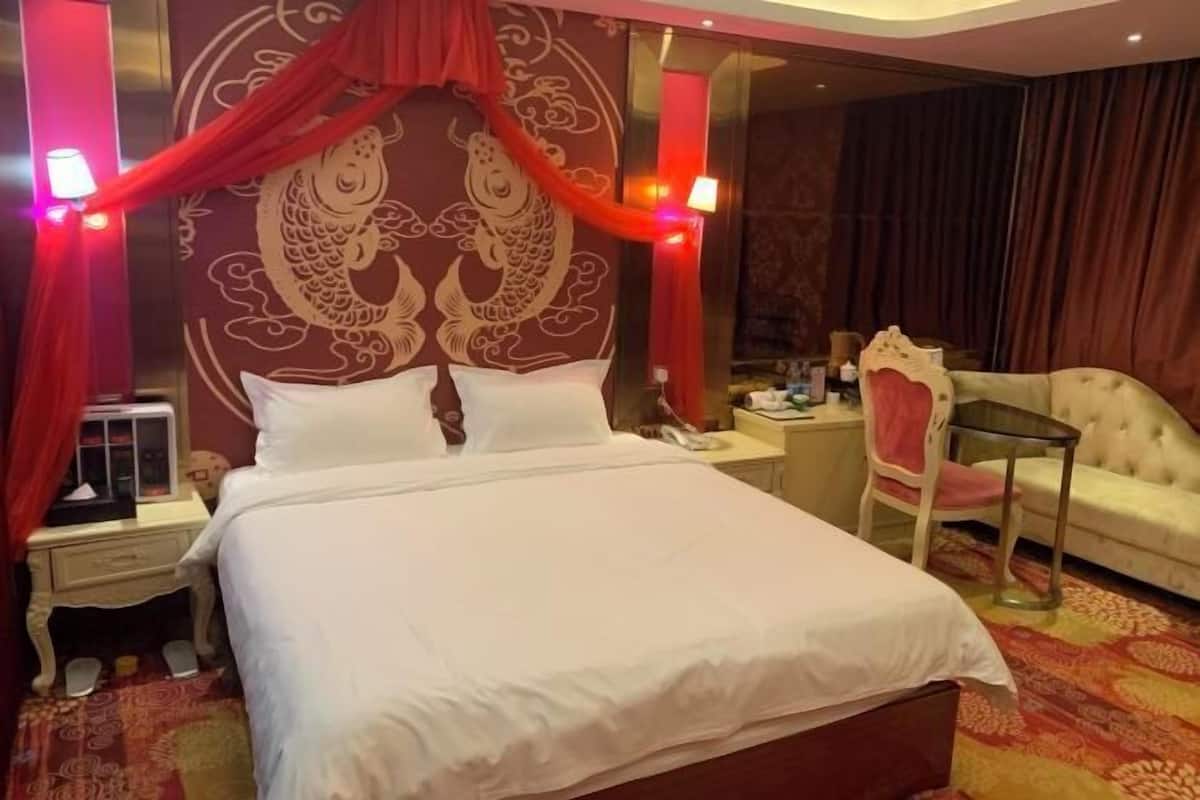 Quarto de hotel com cama grande, uma cadeira, mesa de cabeceira e parede com desenho decorativo de peixe.
