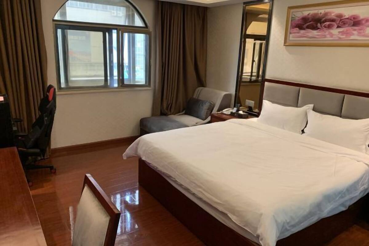 Quarto de hotel com uma cama grande, uma mesa, uma cadeira, uma janela e um quadro na parede.
