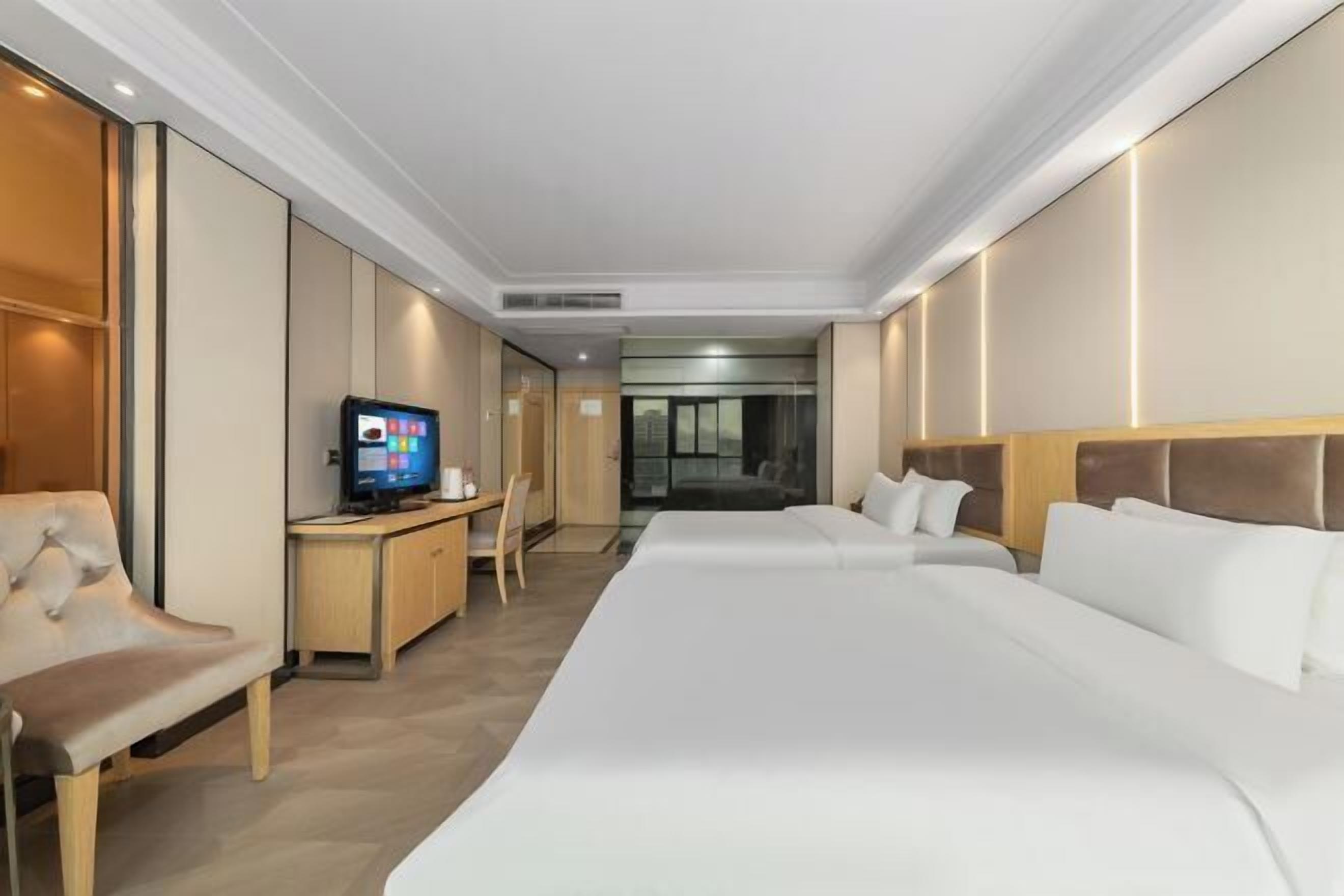 Une chambre d’hôtel avec un grand lit, un bureau avec un ordinateur, une télévision et une vue sur la ville.