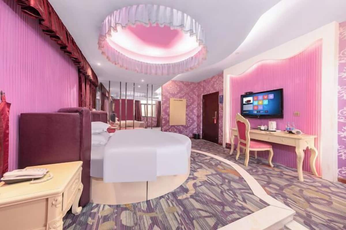 Quarto de hotel com cama, escrivaninha, cadeira, televisão e carpete estampado.