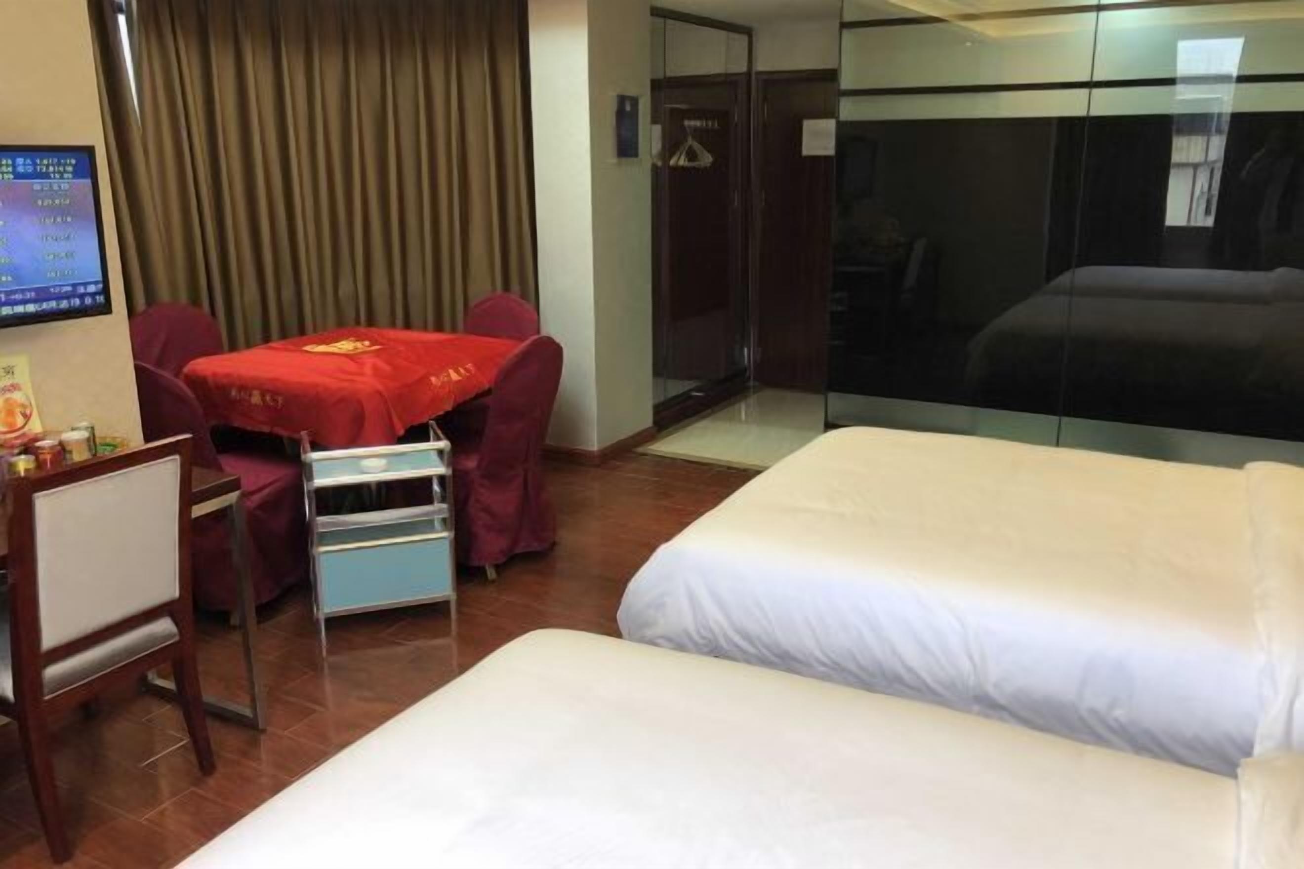 A hotel room with two beds, a small table with a red tablecloth, a TV, and a wardrobe.