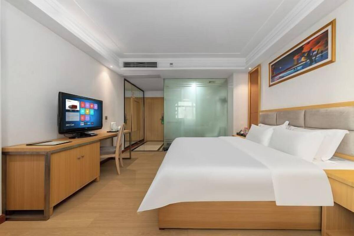 Quarto de hotel com cama, televisão, escrivaninha e cadeira.