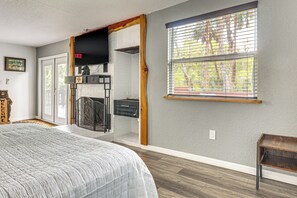 Un dormitorio con cama, chimenea empotrada, ventana con persianas y puerta que da a otra habitación.