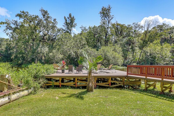A wooden deck with outdoor seating and a view of a lake surrounded by trees.