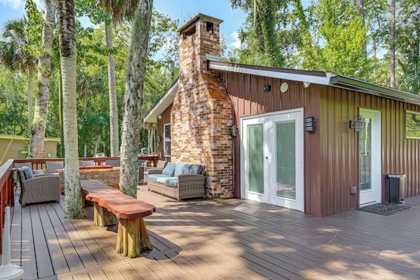 Una terraza de madera con mobiliario exterior, una chimenea de piedra y una puerta de metal.