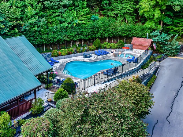 Une piscine entourée d’une terrasse, de chaises longues et d’un petit bâtiment doté d’un toit rouge.