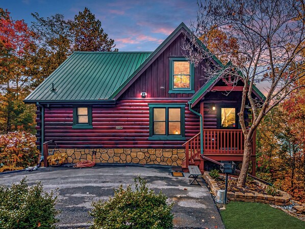 A log cabin with a stone foundation, a green metal roof, and a wooden deck. - Family Cabin Retreat | Multi Arcade | HotTub (Gatlinburg)
