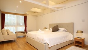 A bedroom with a large bed, a bedside table with a lamp, a chair, and a window with curtains. - Villa Bavaria (Hakuba)
