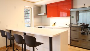 A modern kitchen with a central island, red cabinets, and a stainless steel refrigerator. - Villa Bavaria (Hakuba)