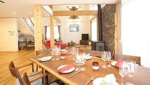A dining area with a wooden table set for a meal, a staircase leading to another room, and a stone wall in the background. - Villa Bavaria (Hakuba)