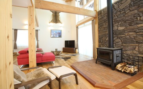 A spacious living room with a stone fireplace, wooden beams, a red sofa, and a television.