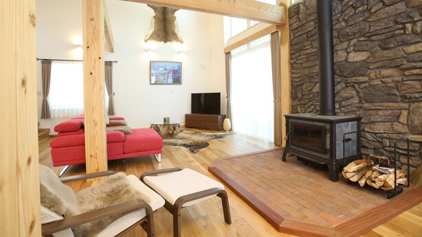 A spacious living room with a stone fireplace, wooden beams, a red sofa, and a television. - Villa Bavaria (Hakuba)