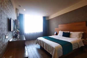 Habitación de hotel con cama, escritorio, televisor de pantalla plana y ventana con cortinas.