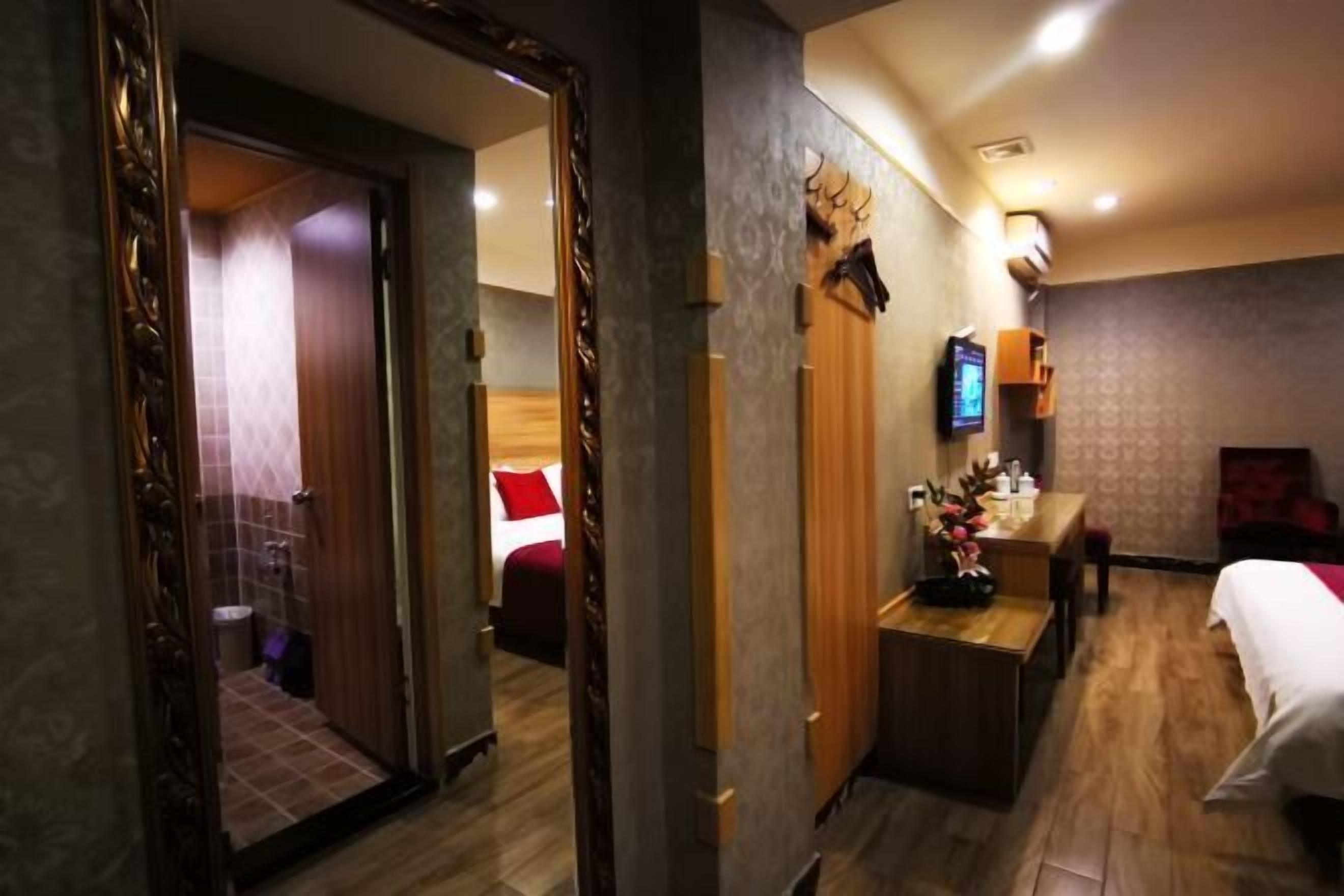 Una habitación de hotel con piso de madera, una cama con ropa de cama blanca, un escritorio con una silla, un televisor y un espejo.
