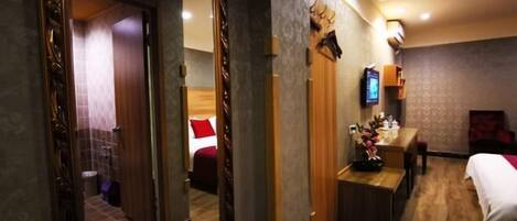 Una habitación de hotel con piso de madera, una cama con ropa de cama blanca, un escritorio con una silla, un televisor y un espejo.