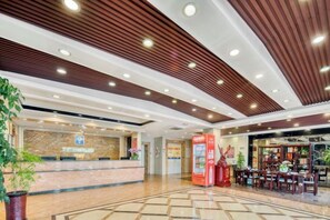 A hotel lobby with a reception desk, a red information kiosk, and a seating area with tables and chairs. - Aiju chain hotel (Yingkou Xiongyue Railway Station) (Yingkou)