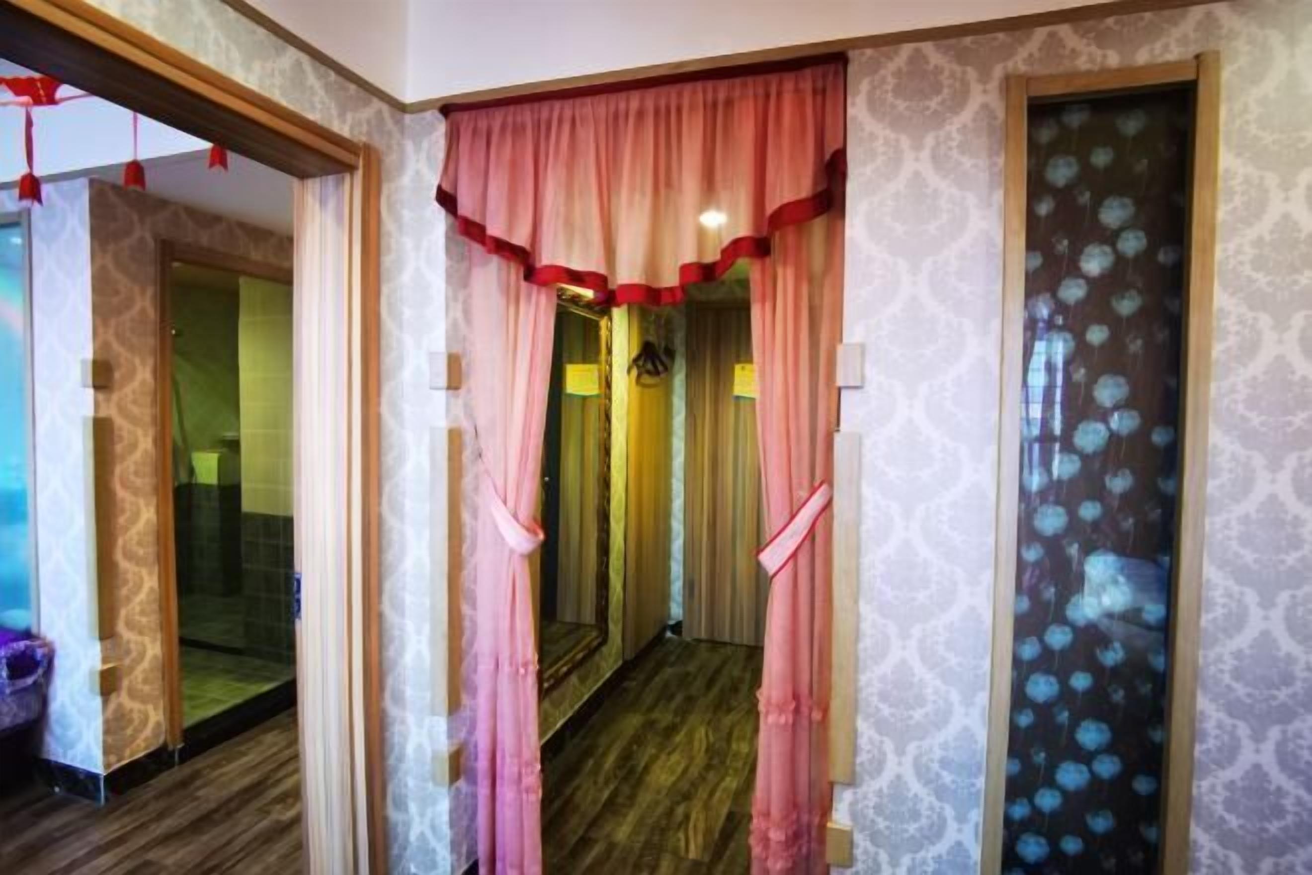 A hallway with patterned wallpaper, a wooden floor, and a door with a mirror.