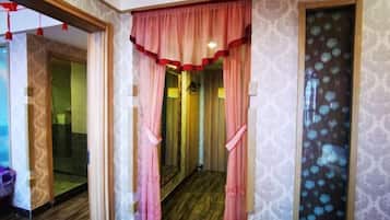 A hallway with patterned wallpaper, a wooden floor, and a door with a mirror.