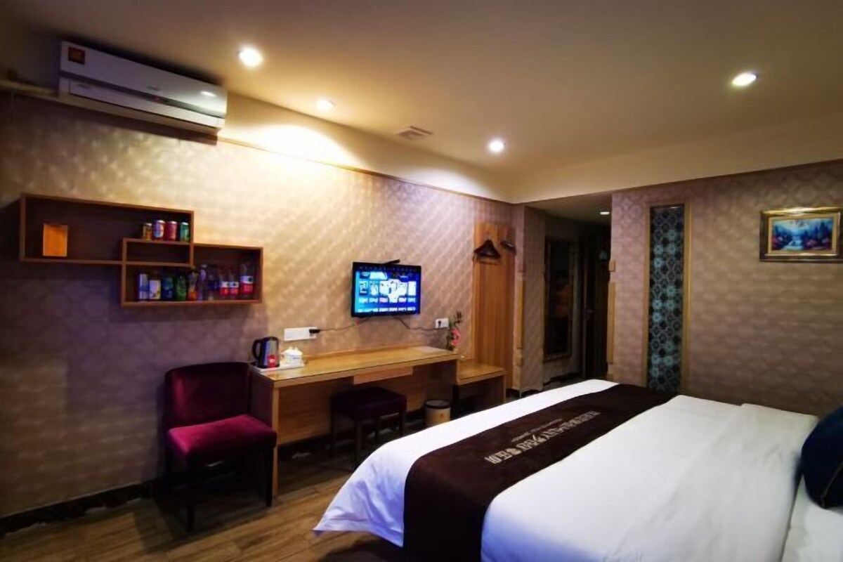 A hotel room with a bed, a desk with a chair, a television, and a shelf with toiletries.