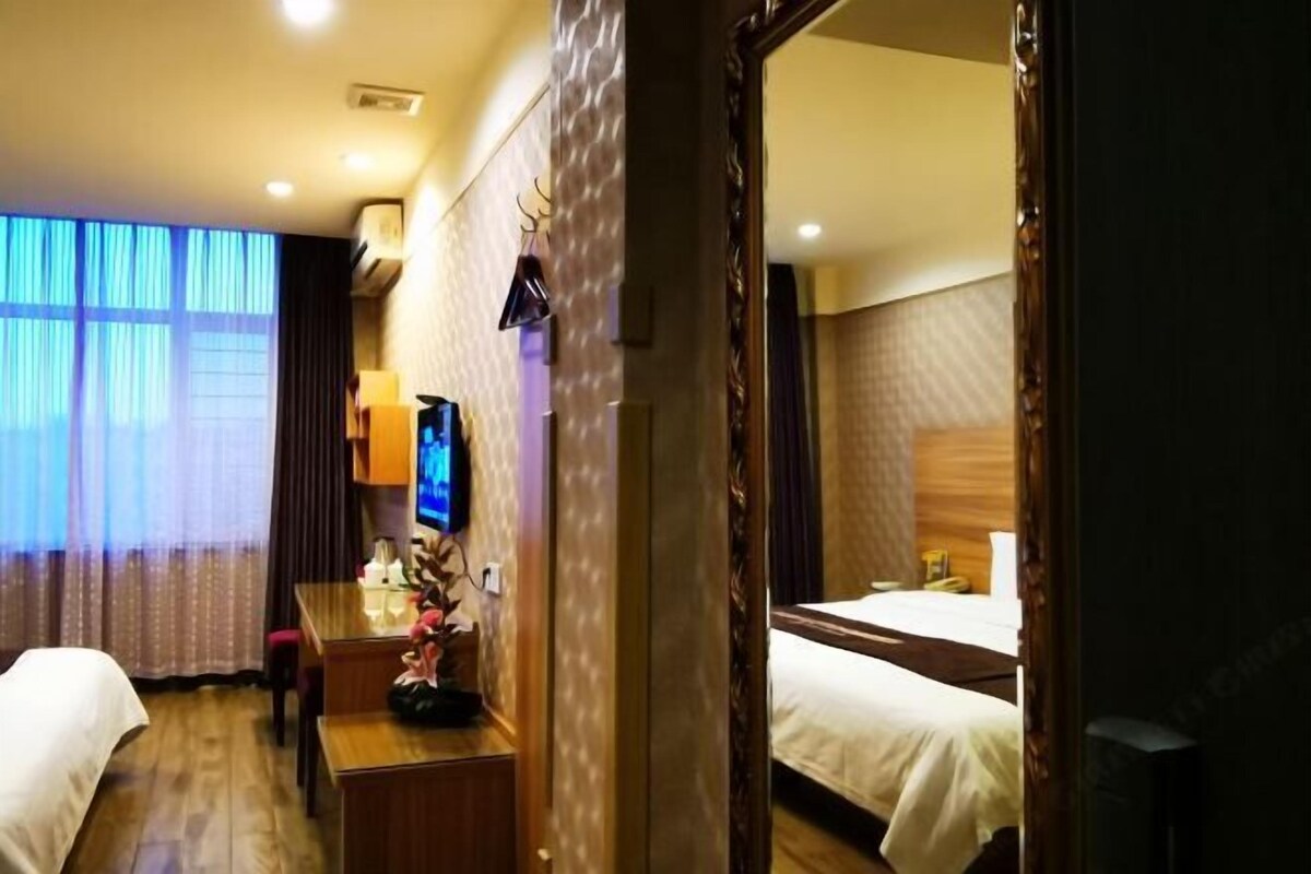 A hotel room with two beds, a desk with a television, and a large mirror.