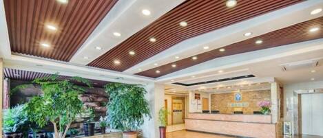 Un vestíbulo de hotel con mostrador de recepción, plantas en macetas y un diseño de techo de madera.