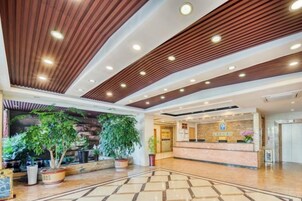 Un vestíbulo de hotel con mostrador de recepción, plantas en macetas y un diseño de techo de madera.