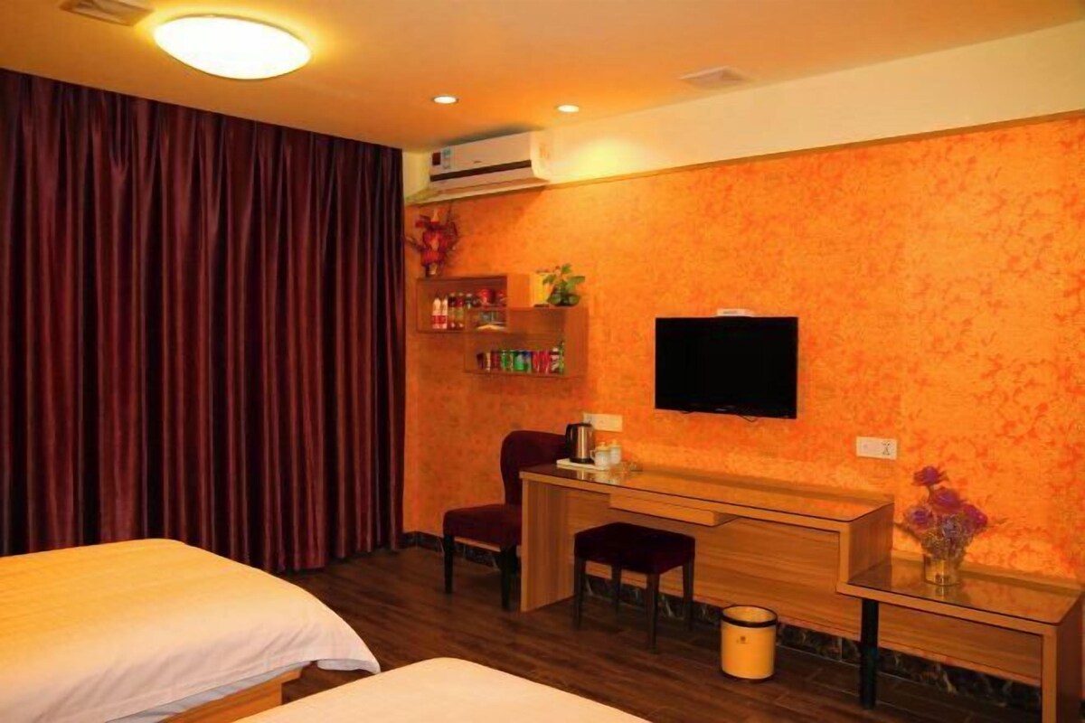 A hotel room with two beds, a desk, a chair, a TV, and a small shelf with toiletries.