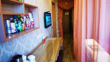 A hotel room with a wooden bench, a TV mounted on the wall, and shelves with various toiletries.
