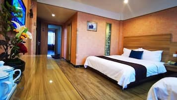 A hotel room with a wooden floor, a large bed with white bedding, a nightstand with a phone, and a wall-mounted TV.
