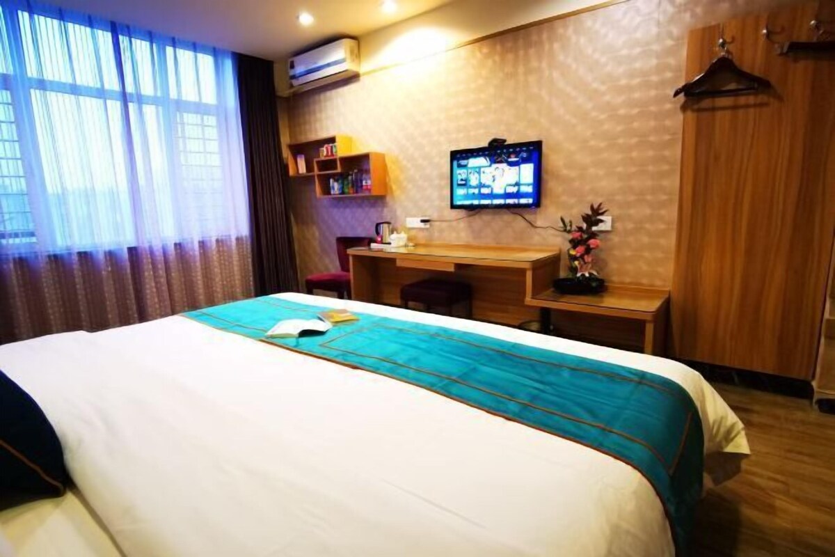 A hotel room with a bed, a desk, a television, and a wardrobe.