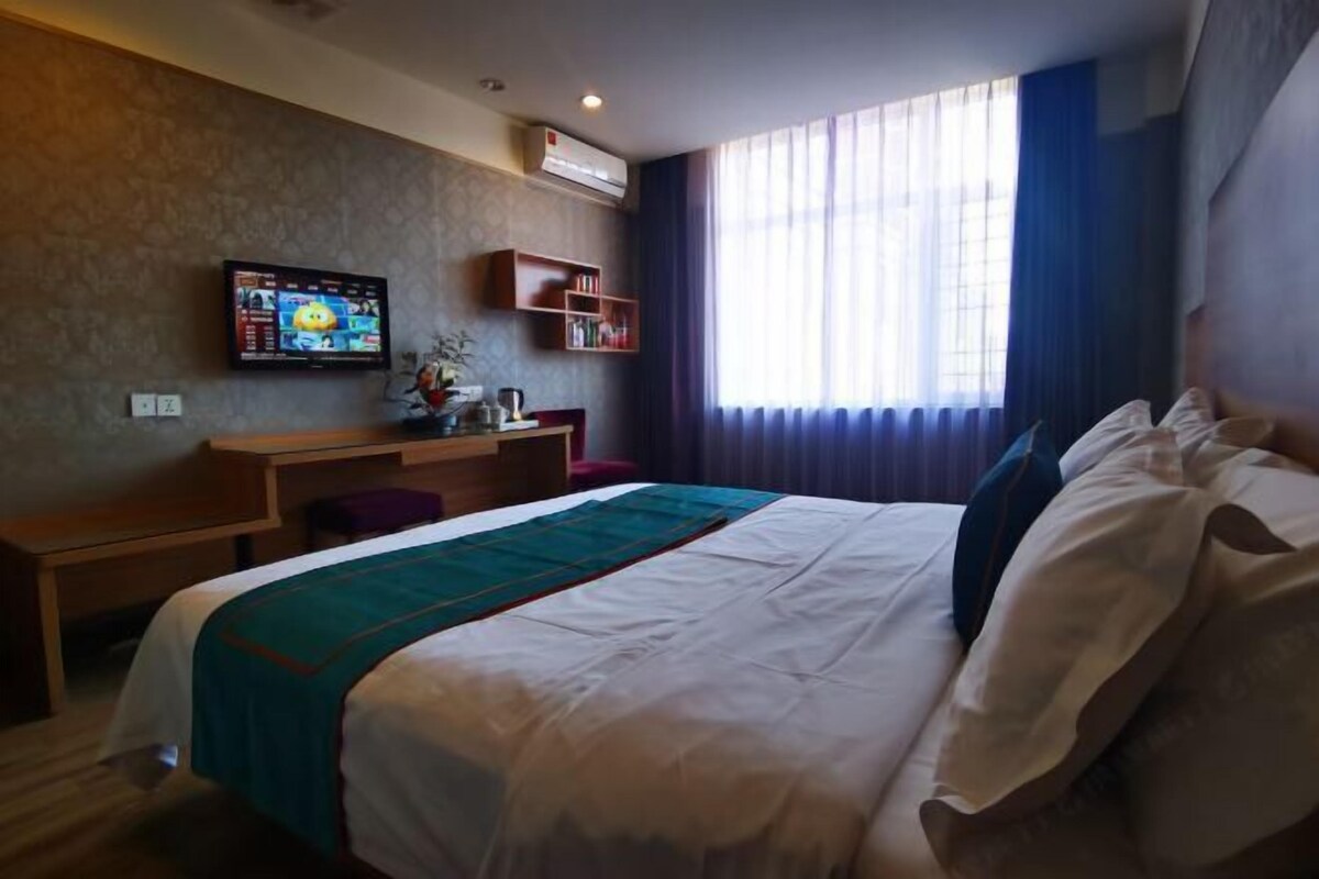 A hotel room with a bed, a desk, a television, and a window with curtains.
