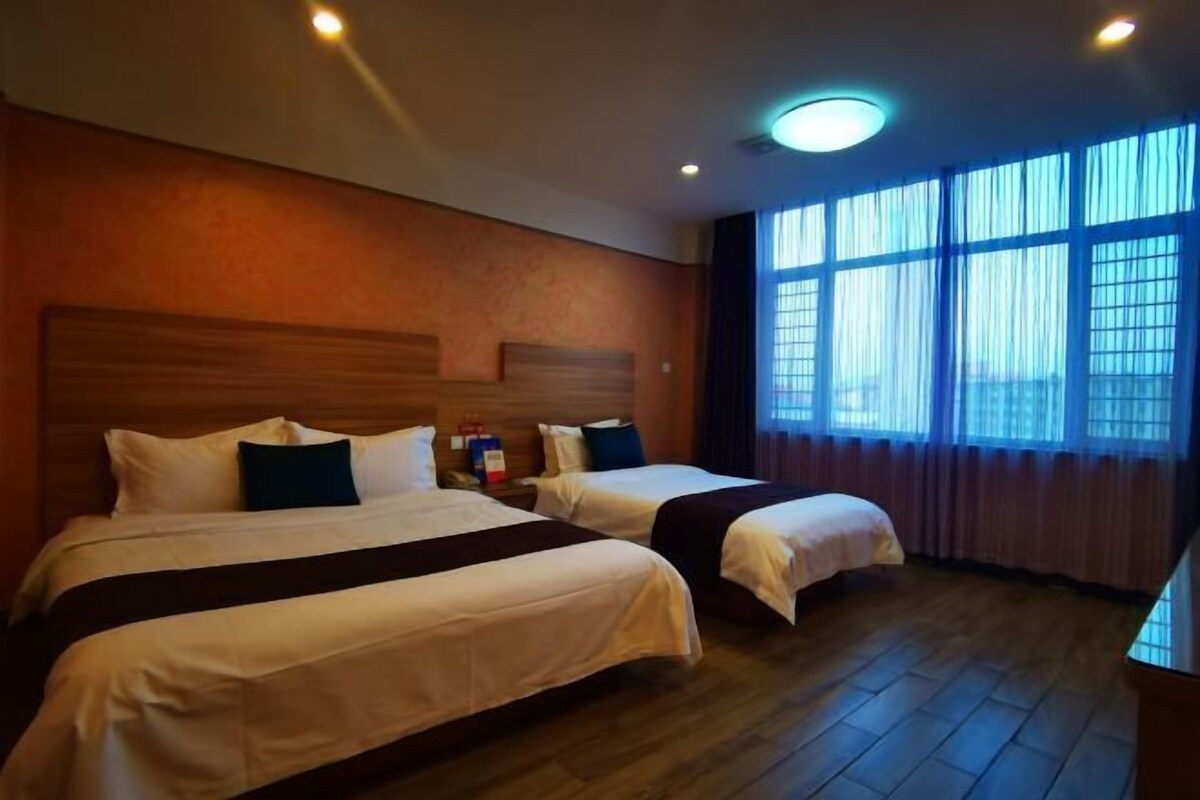 A hotel room with two beds, wooden headboards, a large window with curtains, and a ceiling light.