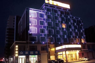 Un edificio de varios pisos con señalización iluminada y ventanas, que cuenta con una entrada a nivel de calle y un automóvil estacionado afuera.