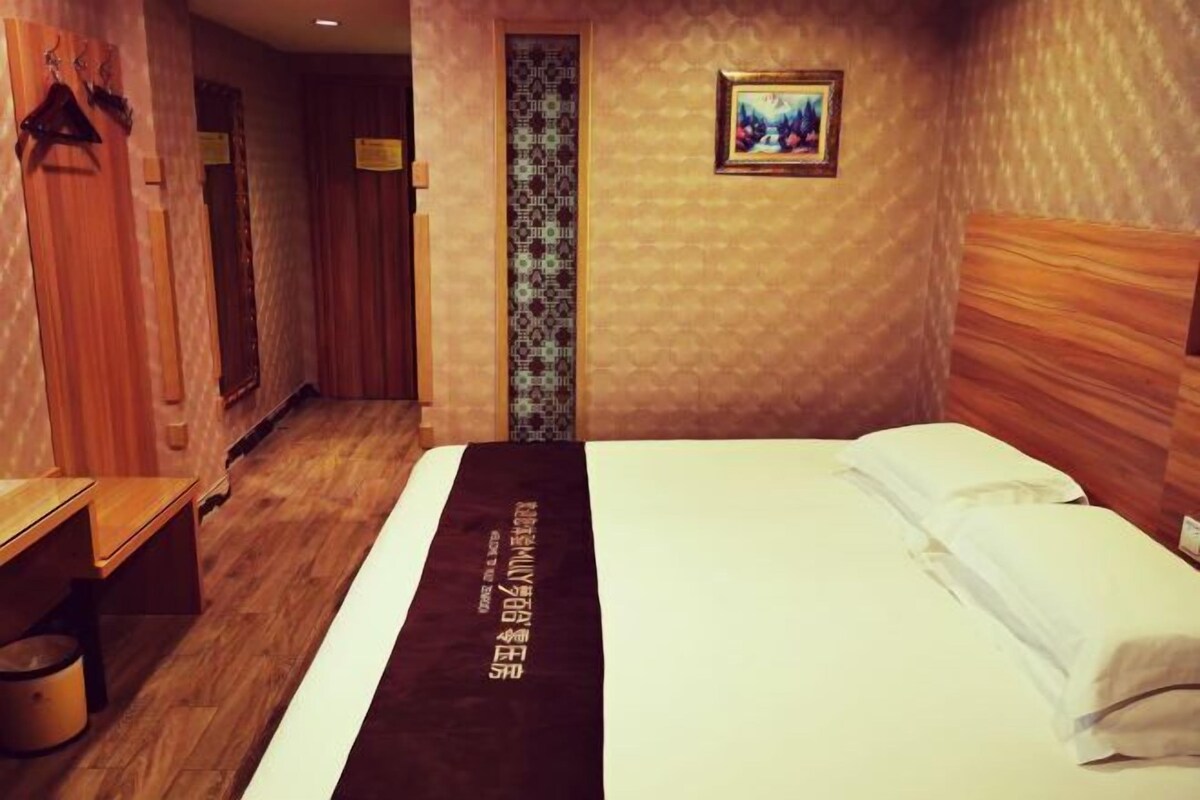 A hotel room with a bed, a bench, a mirror, a patterned wall, and a framed picture.